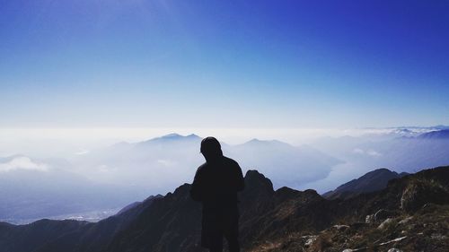 Rear view of silhouette man standing on mountain against sky