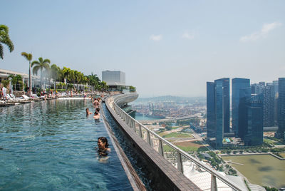 People by swimming pool in city against sky