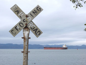 Information sign on wooden post by sea against sky