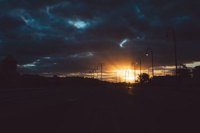 Silhouette city street against sky during sunset