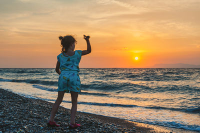 Rear view of girl standing on beach during sunset