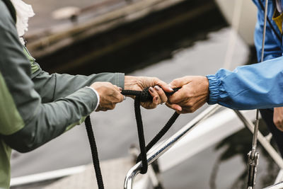 Cropped hands of female instructor and senior man tying rope on yacht's railing