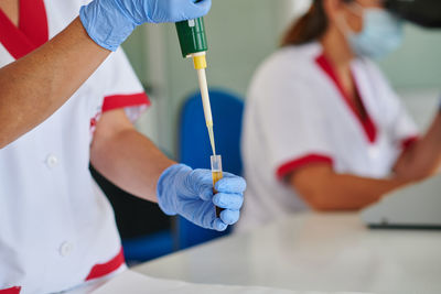 Crop anonymous medical specialist filling sample tube with blood while using pipette in laboratory on light background