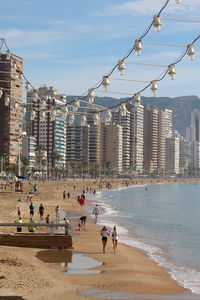 People on beach by city against sky