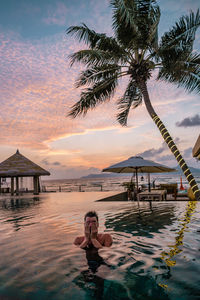 Man in infinity pool against sky at sunset