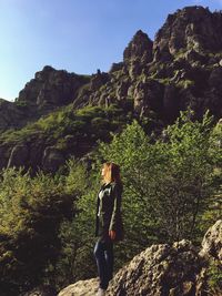 Woman standing on rock by mountain against sky