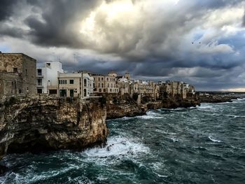 Buildings by sea against cloudy sky