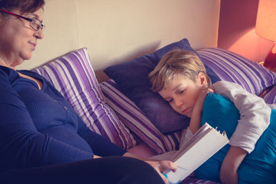 Grandmother reading book for grandson on bed