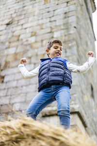 Low angle view of boy flexing muscles while standing against building