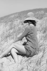 Portrait of young woman sitting on the beach using hat