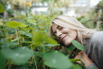 Smiling blond woman smelling plants at garden