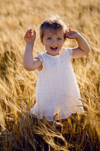 Little girl is happy on the field with ears in the evening sunset in summer.