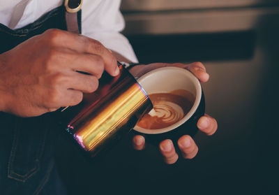 Midsection of barista pouring cream in coffee at cafe