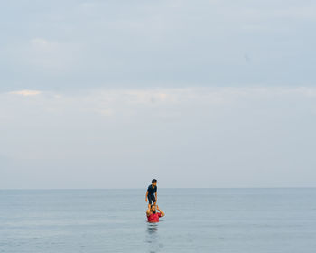 Father carrying son on shoulder in sea against sky