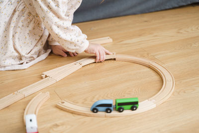 Toddler girl in white dress plays with wooden train at home in the living room