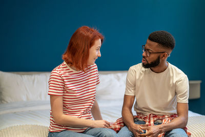 Young interracial couple husband and wife sit on bed at home discussing intimacy issues