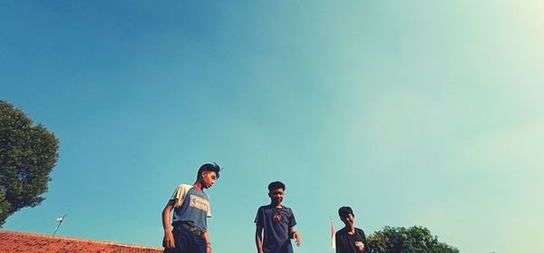 Low angle view of men standing against clear blue sky