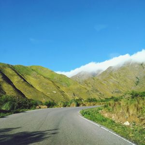 Road amidst green landscape against blue sky