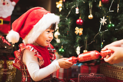 Cropped hand of woman giving gift to girl by christmas tree