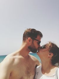 Young couple standing on beach against clear sky
