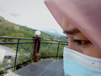 Close-up of young woman wearing mask standing y railing