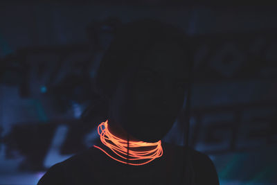 Close-up of woman wearing illuminated necklace in darkroom