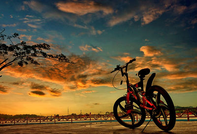 Silhouette bicycle on beach against sky during sunset