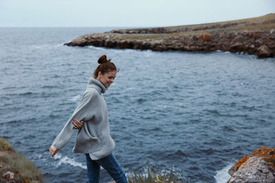 Rear view of woman standing on rock by sea against sky