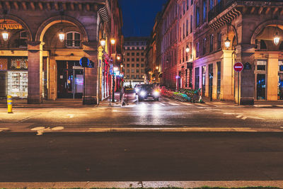 Illuminated street amidst buildings in city at night