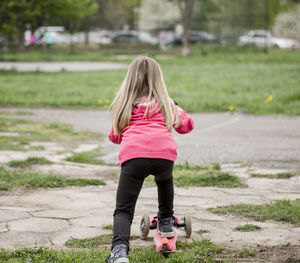 Rear view of girl riding push scooter on footpath 