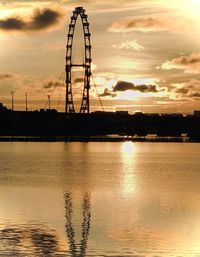 Silhouette ferris wheel by river against sky during sunset