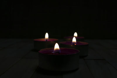 Close-up of lit tea light candles on table in darkroom