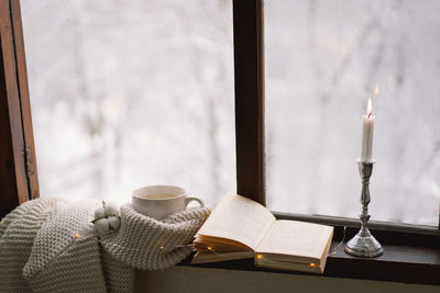 Cup of hot tea and an open book with a warm sweater on a vintage wooden windowsill