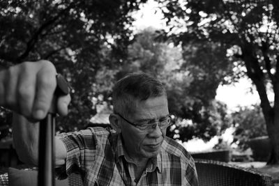 Senior man holding walking cane while sitting against trees