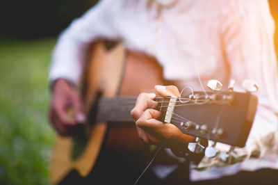 Midsection of man playing guitar in park