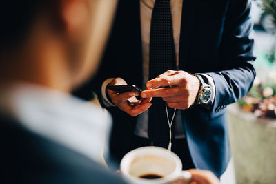 Midsection of businessman using smart phone while standing with colleague drinking coffee at cafe