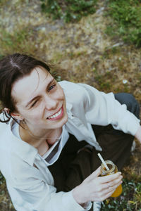 High angle portrait of smiling young non-binary person holding juice bottle