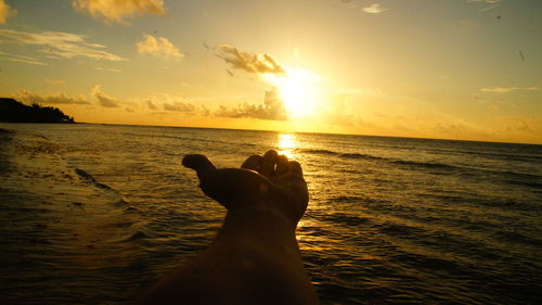 Silhouette hand against sea during sunset