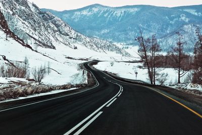 Road by snowcapped mountains against sky