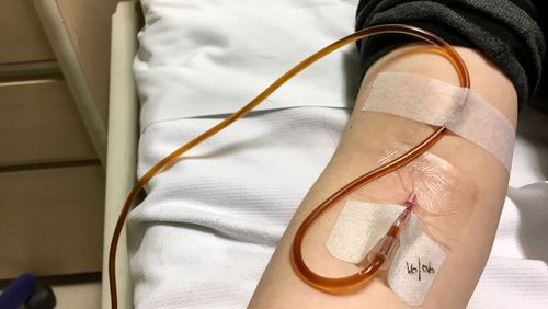 Cropped hand of patient with iv drip on bed in hospital