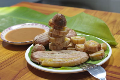 Grilled banana with dipping sauce on wooden table.