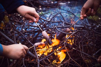 Close-up of people cooking sausages in bonfire