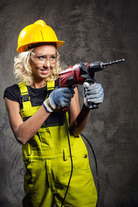 Smiling female worker holding drill while standing against wall