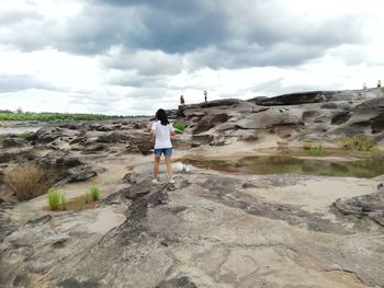 Rear view of woman standing on rock against sky