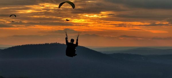 Silhouette person paragliding against sky during sunset