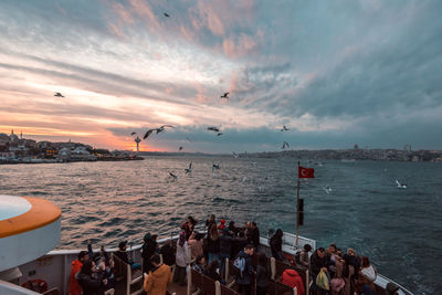 Group of people on sea against sky during sunset