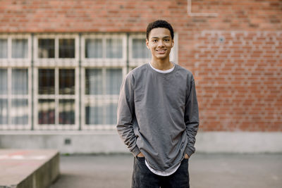 Portrait of smiling male student standing with hands in pockets in high school campus