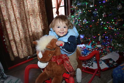 Portrait of girl sitting on rocking horse by christmas tree at home