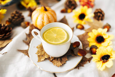 Ceramic cup of lemon tea surrounded by sunflowers, pumpkins, leaves, acorns, pine cones