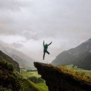 Man jumping over mountain against cloudy sky during foggy weather